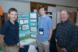 Two students and teacher standing beside their STEM fair exhibit